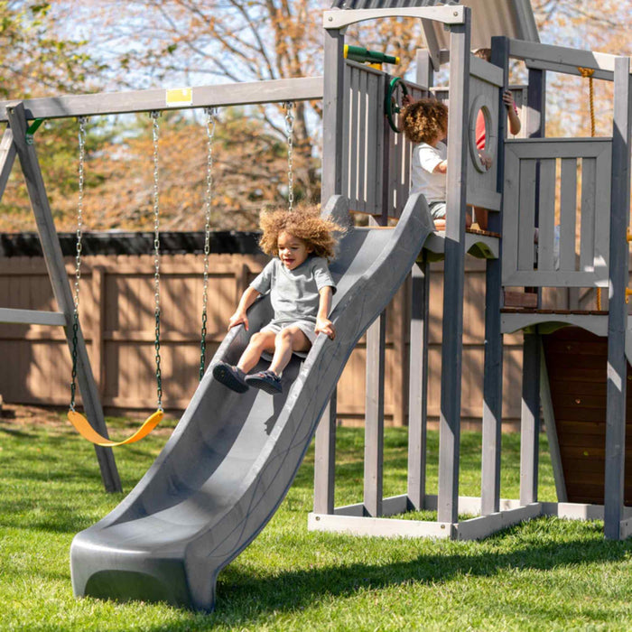 Jack and June Haven 2 Outdoor wooden playset with swing and slide, climbing ramp with rope and undercover landing. View of child sliding down the slide